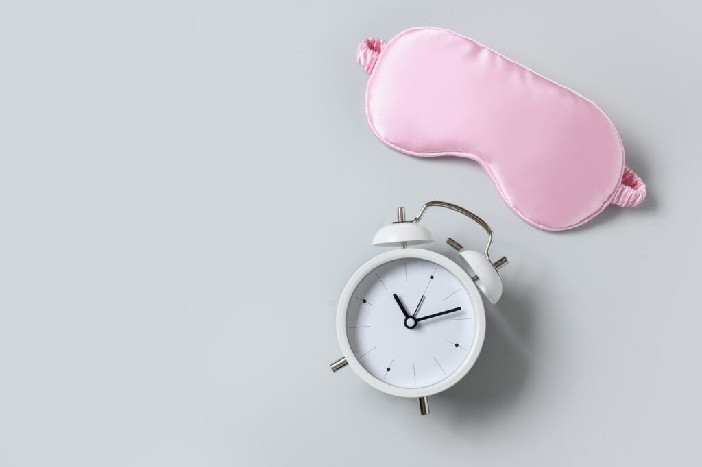 Pink sleeping mask, watch and vitamins capsules. Concept of sleep, health care, daily routine.